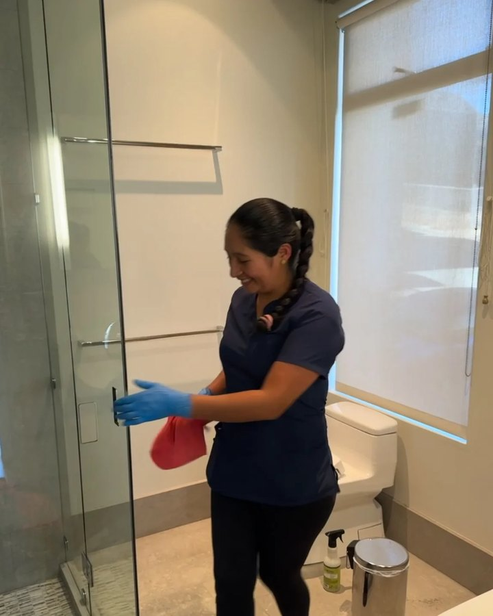Royal Glow team member detailing a glass shower door with a color-coded cloth