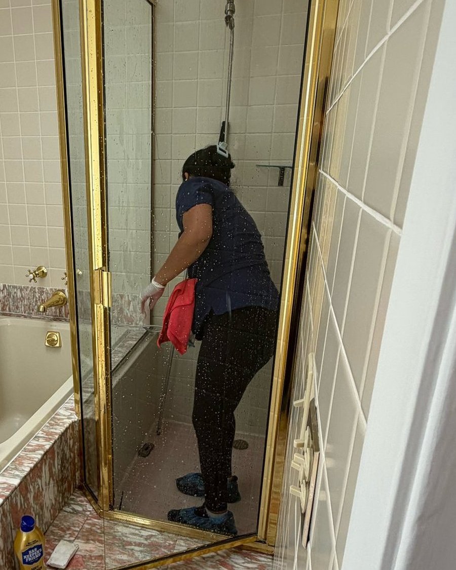 Royal Glow Cleaning team member polishing a glass shower door